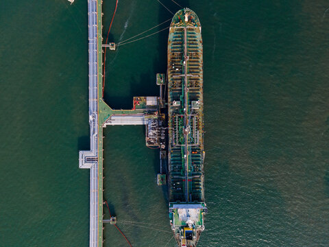 Aerial view of a large oil tanker docked at an industrial pier in the sea, showing the ship's deck and the long jetty structure in Cilacap Regency, Central Java, Indonesia.