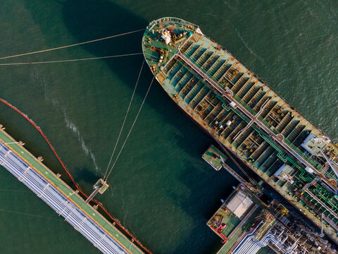 Aerial view of a large tanker ship moored at an industrial terminal with pipelines and mooring lines visible in the water in Cilacap Regency, Central Java, Indonesia.