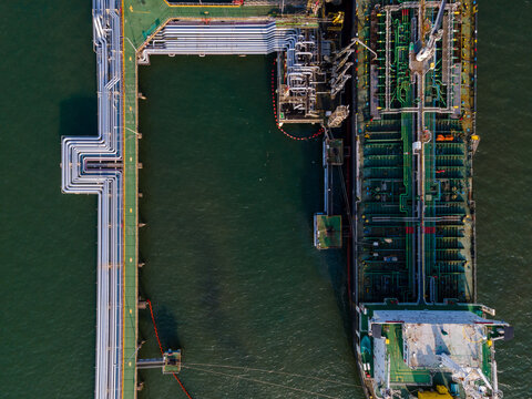 Aerial view of an oil tanker docked at a terminal with industrial pipelines and storage infrastructure in Cilacap Regency, Central Java, Indonesia.