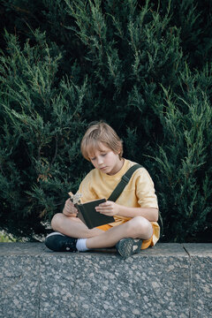 Young boy sits on a stone wall and reads a book outdoors