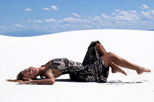 Young woman in a black and white dress lies on white sand dunes