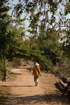 Person in conical hat walks on dirt path in rural village