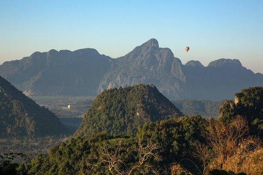 Hot air balloons float over lush green mountain valley