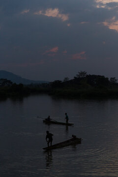 Silhouettes of people in canoes on a tranquil river at dusk
