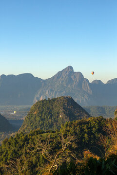Hot air balloons float over a lush mountain landscape