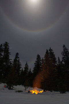 Lunar halo and stars above a winter campfire