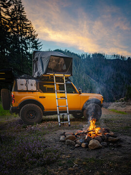 Yellow overland vehicle with tent parked by a campfire