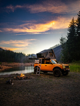 Orange overlanding truck camping by a lake at sunset