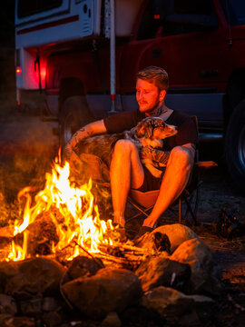 Young tattooed man relaxes by campfire with his dog