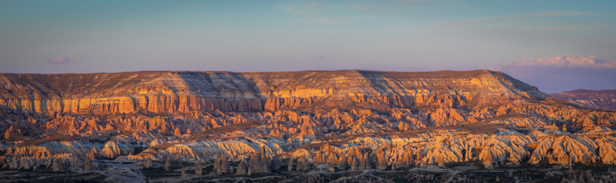 Aerial view of Rose Valley featuring unique fairy chimneys and rugged rock formations illuminated by golden hour light in Goreme, Nevsehir, Turkiye.