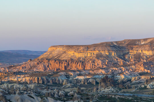 Aerial view of Rose Valley in Cappadocia, featuring unique rock formations, fairy chimneys, and rugged terrain illuminated by the soft light of the golden hour in Goreme, Nevsehir, Turkiye.