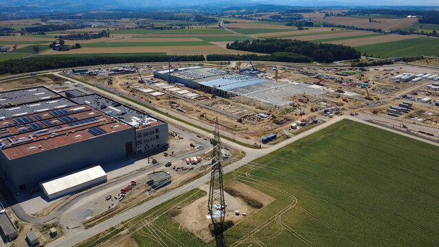 Aerial view of a data center construction site with large industrial buildings, heavy machinery, and surrounding agricultural fields in Kronstorf, Upper Austria, Austria.