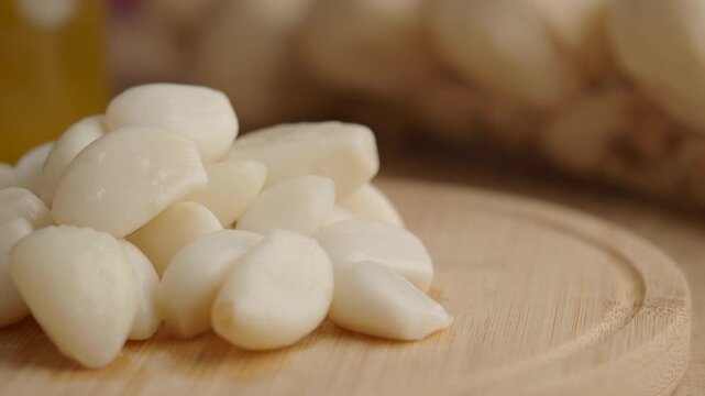 Close up rotation of fresh peeled garlic cloves on wooden cutting board with blurred pantry background