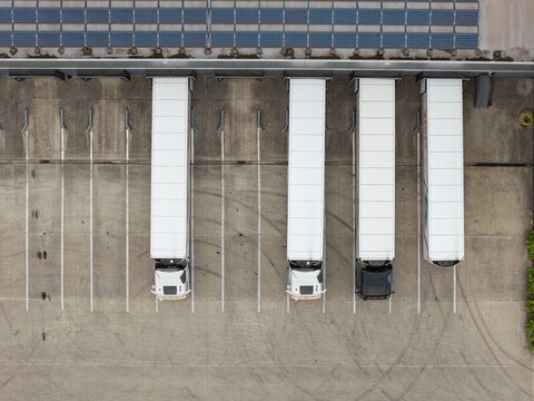 Aerial view of semi-trucks parked at a modern distribution center loading dock with solar panels installed on the warehouse roof in Genk, Flanders, Belgium.