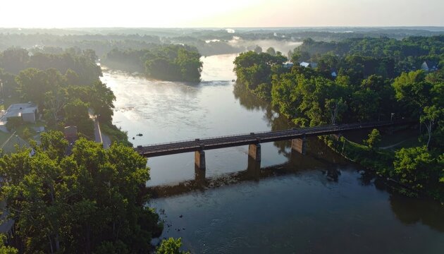 Aerial view of a railway bridge over a misty river at sunrise.