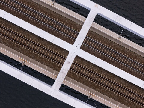Aerial view of a railway bridge with parallel tracks and white structural beams crossing over dark water in Gdansk, Poland.