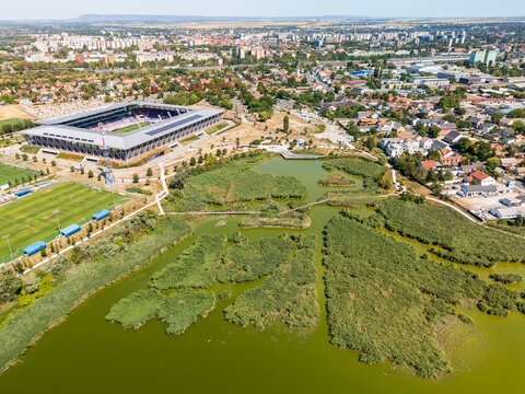Aerial view of Sostoi Stadion in Szekesfehervar, Hungary, beside Sosto lake and parkland, with football pitch, grandstands and surrounding urban landscape.