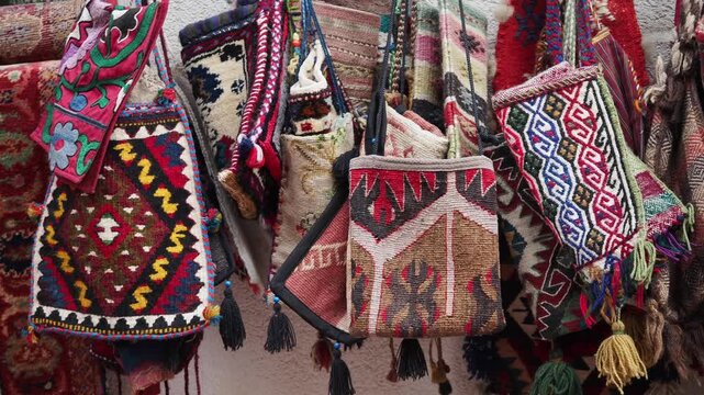 Colorful handmade woven bags hang in market displaying intricate traditional patterns and tassels