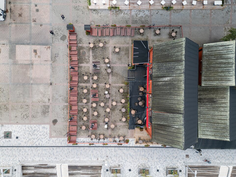 Aerial view of an empty restaurant patio with tables and chairs arranged on a paved surface next to a building with a dark roof in Oulu, North Ostrobothnia, Finland.