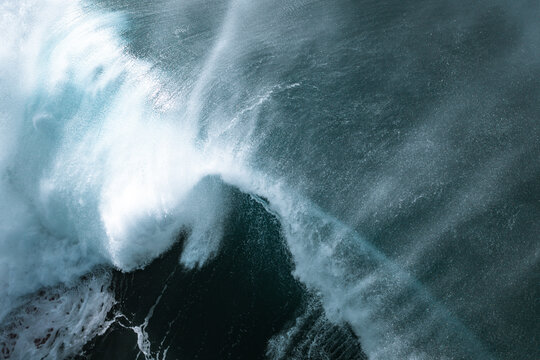 Aerial view of a large ocean wave breaking with white foam and spray in the deep blue sea at Narrabeen, New South Wales, Australia.