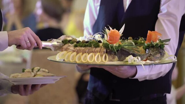 Waiter In Uniform Serving Elaborately Garnished Stuffed Baked Fish From Silver Platter To Guests At Formal Banquet