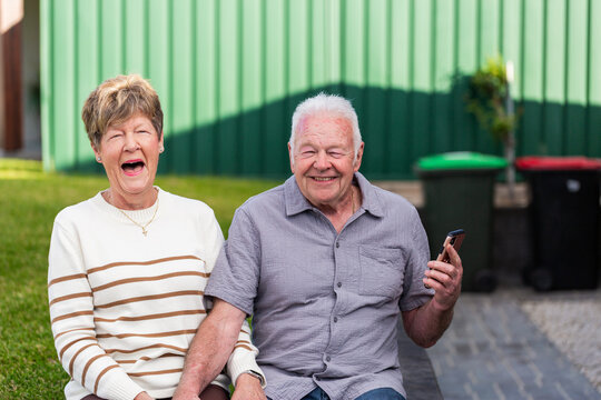 laughing Australian couple together outside holding mobile phone