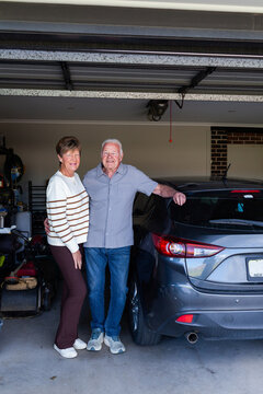 portrait of happy senior couple together in their garage beside car
