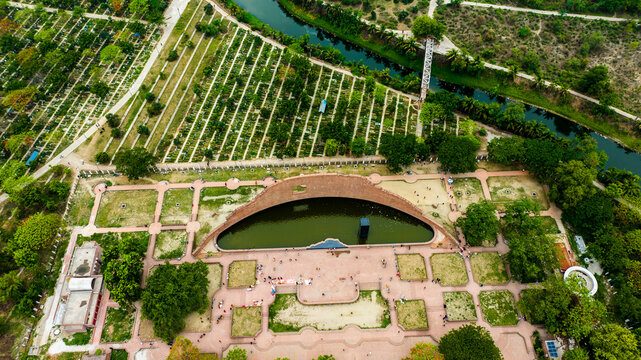 Aerial view of the Rayer Bazaar Martyred Intellectuals Memorial with its curved brick wall and reflecting pool, surrounded by greenery and pathways in Dhaka, Dhaka Division, Bangladesh.