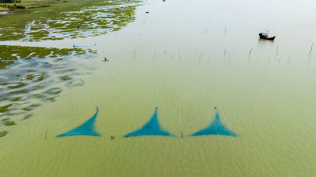 Aerial view of fishing nets submerged in the water with a small boat nearby and green marshland along the coast in Patharghata, Barisal Division, Bangladesh.