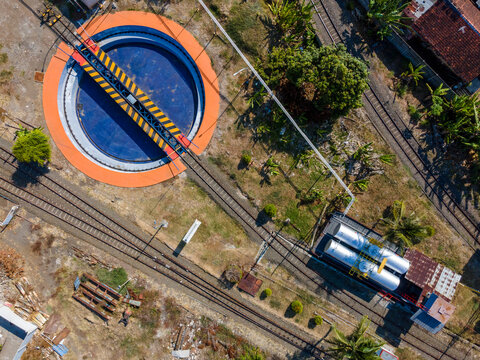 Aerial view of a railway turntable with a rotating bridge and tracks surrounded by storage tanks and vegetation in Cilacap, Central Java, Indonesia.