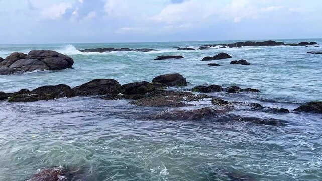 Strong Ocean Waves Crashing Over Dark Lava Rocks along Kanyakumari Beach Shore.  Turquoise Sea Water Swirling Across Black Coral Rocks in Kanyakumari.