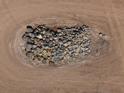 Aerial view of a large pile of rocks and boulders situated in the center of a cleared dirt field with visible tire tracks in Kilsyth, Victoria, Australia.