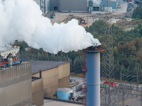 Aerial view of the industrial manufacturing facility at Genk-Zuid Rechteroever with a tall chimney emitting smoke, surrounded by industrial infrastructure in Genk, Vlaanderen, Belgium.