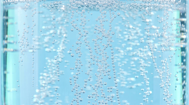 Bubbles rising through blue liquid in glass container create bright abstract aquatic background with refreshing movement and texture