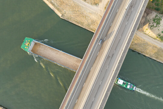 Aerial view of a cargo barge navigating the canal under a bridge at Haven Genk, Genk, Vlaanderen, Belgium.