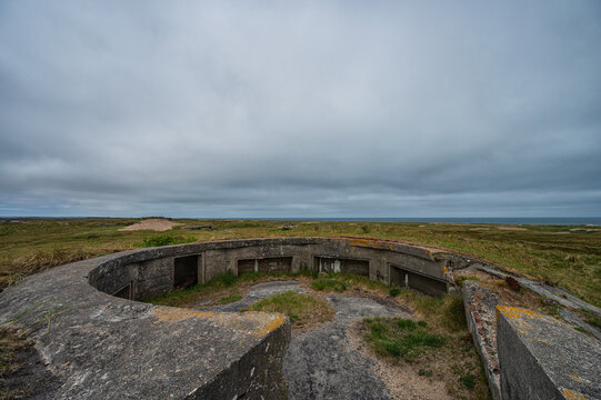 Open concrete gun emplacement at German WW2 Hanstholm I coastal battery in Denmark. Abandoned military fortification of Atlantic Wall overlooking grassy landscape and sea under cloudy sky.