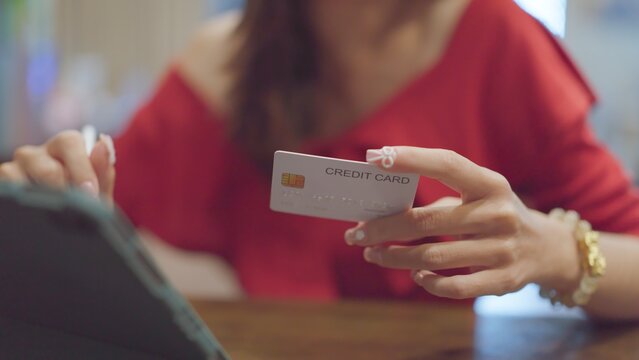 Asian woman holding credit card enters payment data inside tablet, purchasing retail items online, verifying digital banking account balance, completing safe ecommerce checkout transaction indoors.