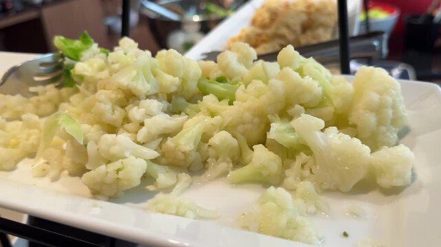 Close-up video of cooked cauliflower floret on white platter with fork ready for healthy buffet meal