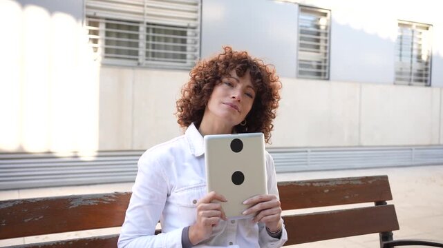 A Young Woman Engaged with Her Tablet While Sitting Comfortably Outdoors in an Urban Environment