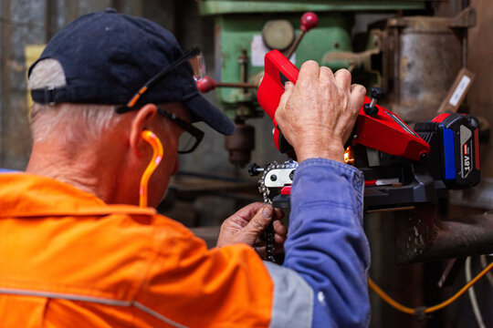 handyman in his fifties sharpening chainsaw teeth with electric sharpener tool in shed