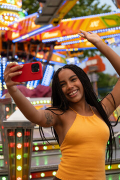 Smiling young woman capturing selfie moment at a vibrant amusement park