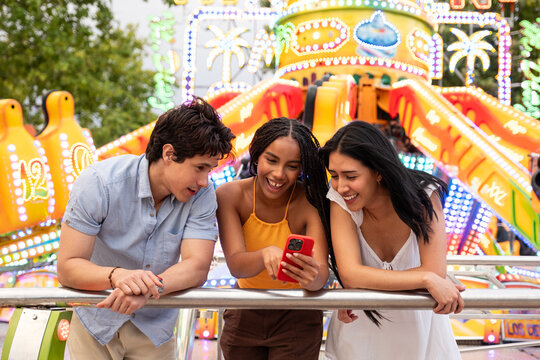 Diverse friends sharing a laugh while watching content on a smartphone at a fair