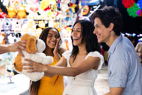 Three happy friends celebrating winning a stuffed animal at a carnival game