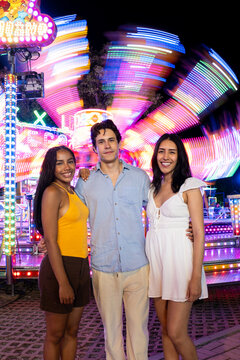 Diverse friends smiling and posing together at a vibrant night fair with amusement rides