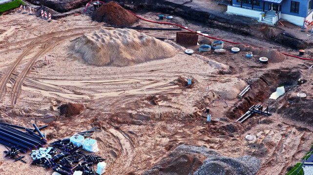 Aerial view of a construction site featuring piles of sand, excavated trenches, and various pipes laid out on the ground in Latvia.