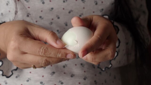Person peeling a white egg with hands in close up motion