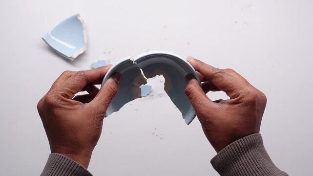 Hands holding broken pieces of light blue ceramic dish on white background