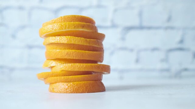 Stack of fresh orange slices filmed in cinematic motion on a white table against a brick wall