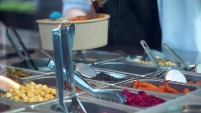 Gloved hands adding food to a take-out bowl from a serving station