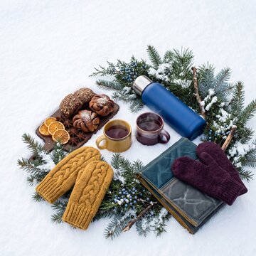Winter picnic with warm drinks, thermos, wool mittens and pastries arranged on fresh snow for cozy seasonal travel, outdoor relaxation and winter getaway concept